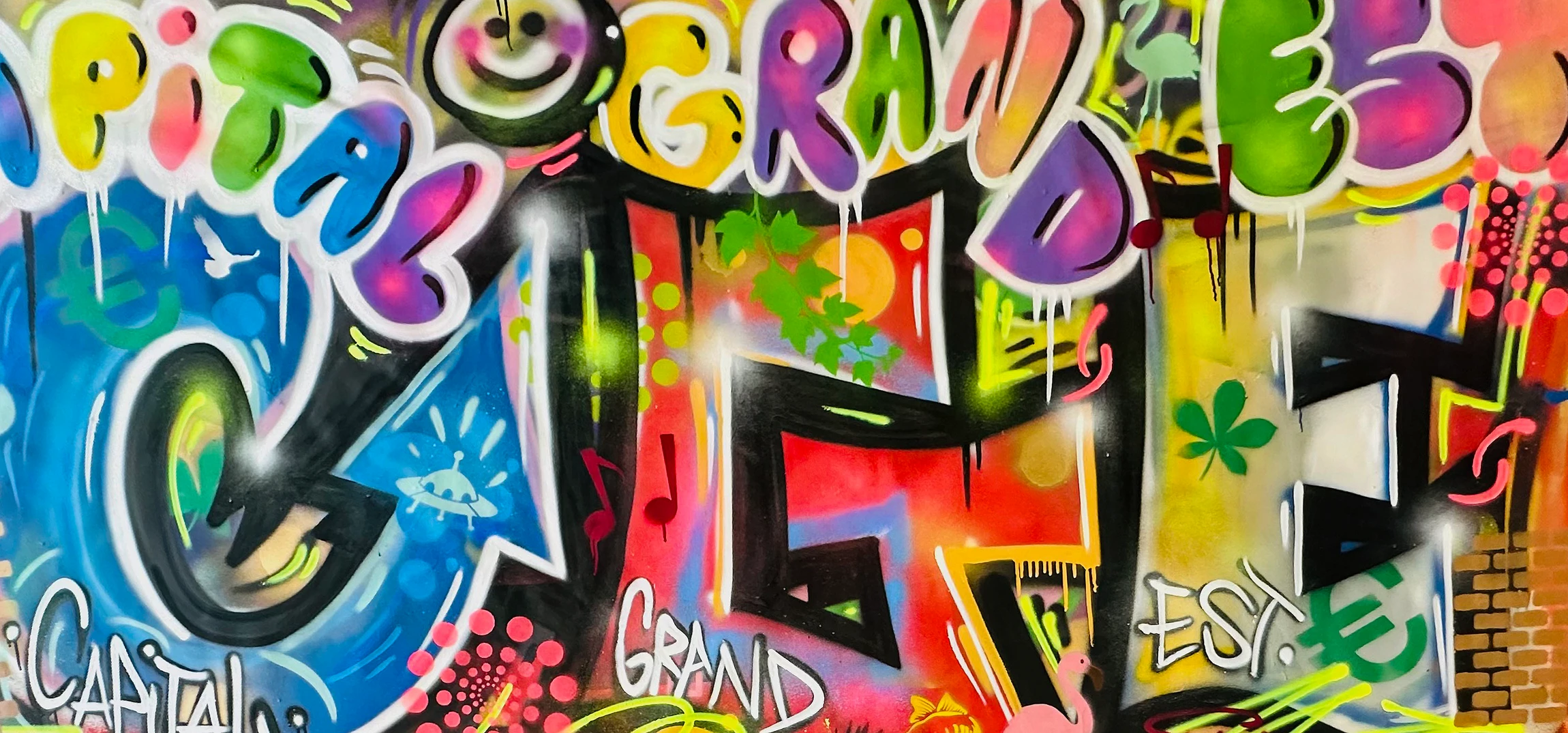 Photographie réaliste d'un artiste-peintre en train de réaliser une fresque murale colorée et graphique sur la façade d'un bâtiment professionnel. L'artiste, vue de dos ou en mouvement, tient ses outils (pinceaux, bombes de peinture), concentré sur son travail. La fresque montre des motifs urbains modernes, des formes géométriques ou abstraites dynamiques, dans une palette de couleurs harmonieuse. Le cadre révèle l'environnement urbain (façade, contexte architectural), la précision du geste artistique, et témoigne du savoir-faire technique et professionnel de l'atelier.