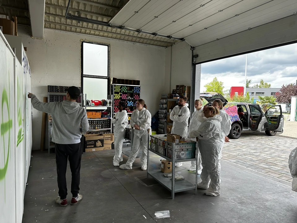 Vue arrière de jeune peintre beau en dungarees blancs, t-shirt bleu, casquette et gants peignant un mur avec un rouleau de peinture