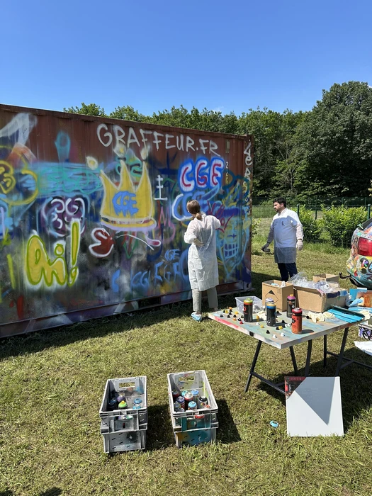 Jeune homme souriant en sweat-shirt à capuche jaune tenant une bombe de peinture aérosol jaune, pointant l'objet vers l'appareil photo dans un geste dynamique et enthousiaste sur fond gris neutre
