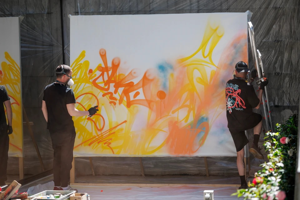Femme artiste blonde en salopette bleue peignant une fresque murale colorée à motifs culturels variés