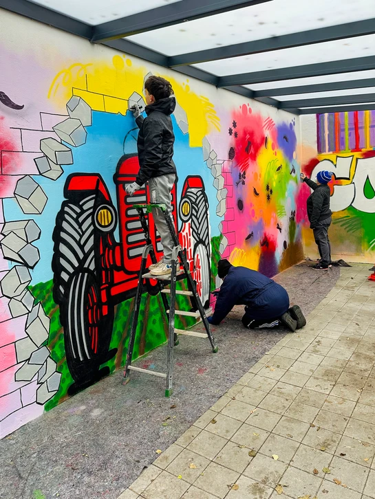 Un artiste urbain professionnel en train de travailler sur une fresque murale en intérieur d'entreprise. L'artiste est équipé de matériel de street art (pinceau, spray ou marqueur) et réalise une création graphique soignée sur un mur blanc ou coloré, montrant à la fois sa maîtrise technique et sa concentration créative. L'environnement doit suggérer un cadre professionnel (ex. mur d'entreprise, atelier). L'image doit transmettre simultanément la créativité artistique et la précision professionnelle, sans texte ni logo visible.