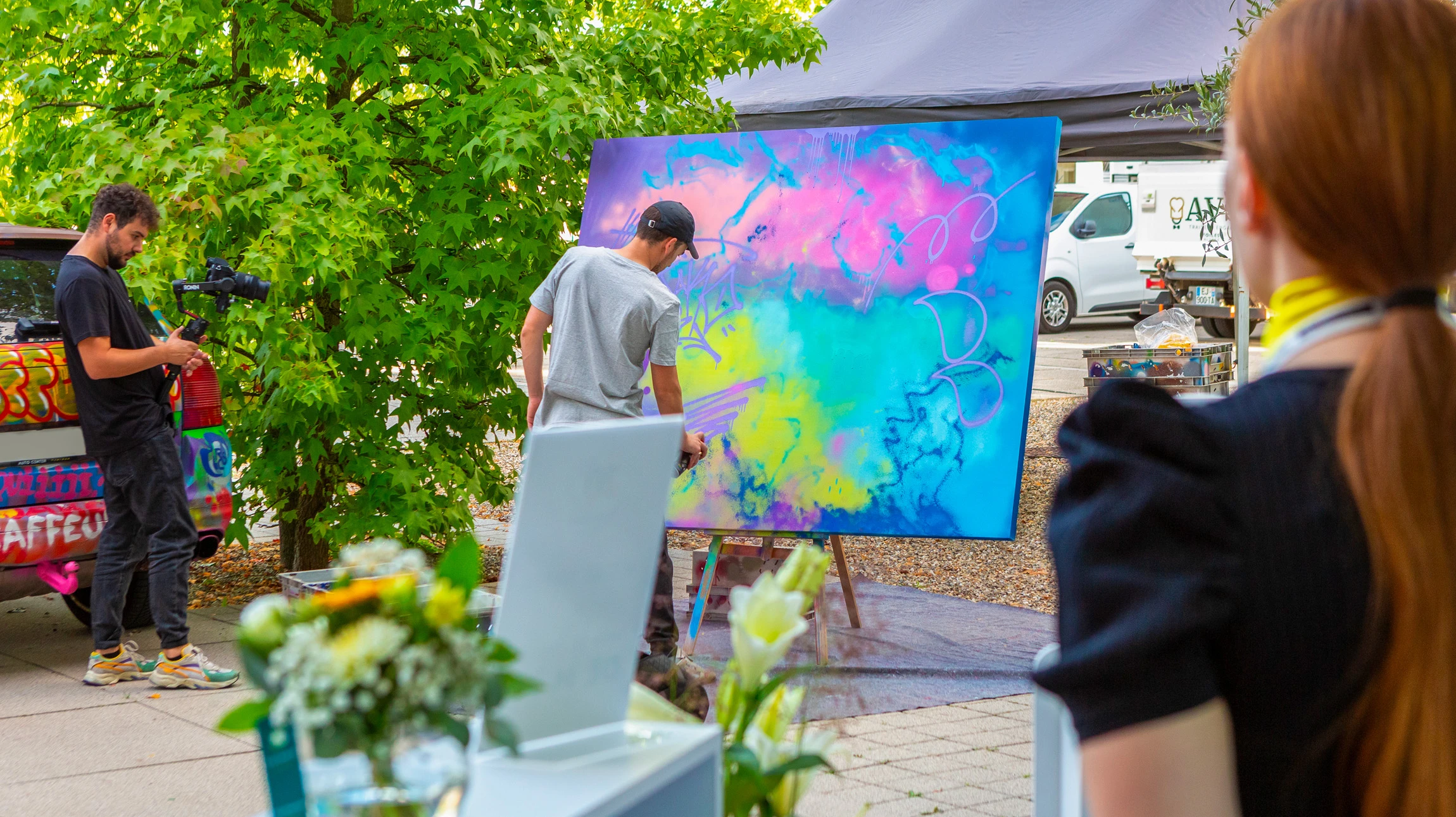 Photographe professionnelle en plan dynamique d'un artiste muraliste en direct pendant une performance live painting. L'artiste est capturé en pleine action avec ses outils (pinceau, bombe de peinture ou rouleau), appliquant de la peinture de couleur sur un mur blanc ou urbain, montrant claramente le processus créatif en temps réel. L'ambiance est professionnelle et spectaculaire, avec un éclairage qui valorise la peinture fraîche et le geste artistique. Le contexte peut être événementiel avec un cadre urbain ou architectural reconnaissable. L'image transmet dynamisme, expertise technique et l'essence du live painting comme performance artistique professionnelle.