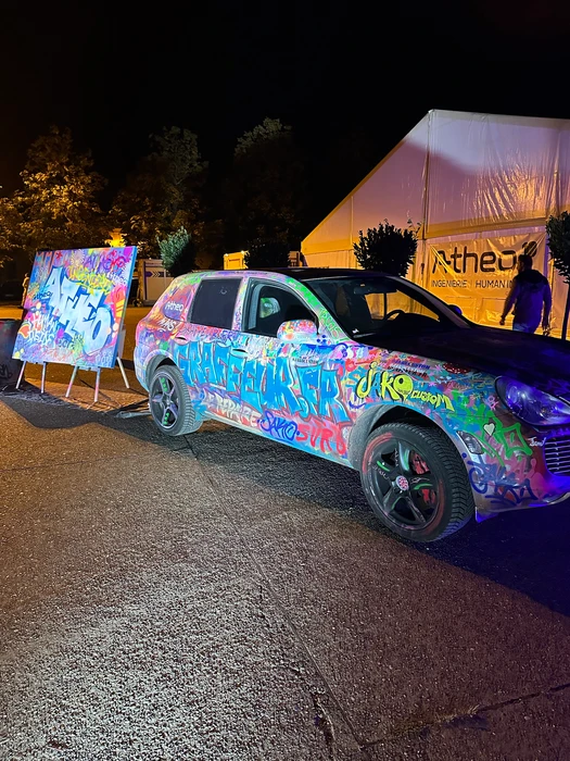 Un artiste en train de créer une fresque murale détaillée à la bombe aérosol ou au pinceau sur une grande surface urbaine, montrant des traits colorés et dynamiques en cours de réalisation, avec en arrière-plan un environnement urbain ou de chantier professionnel, capturant le processus créatif et la maîtrise technique du live painting.