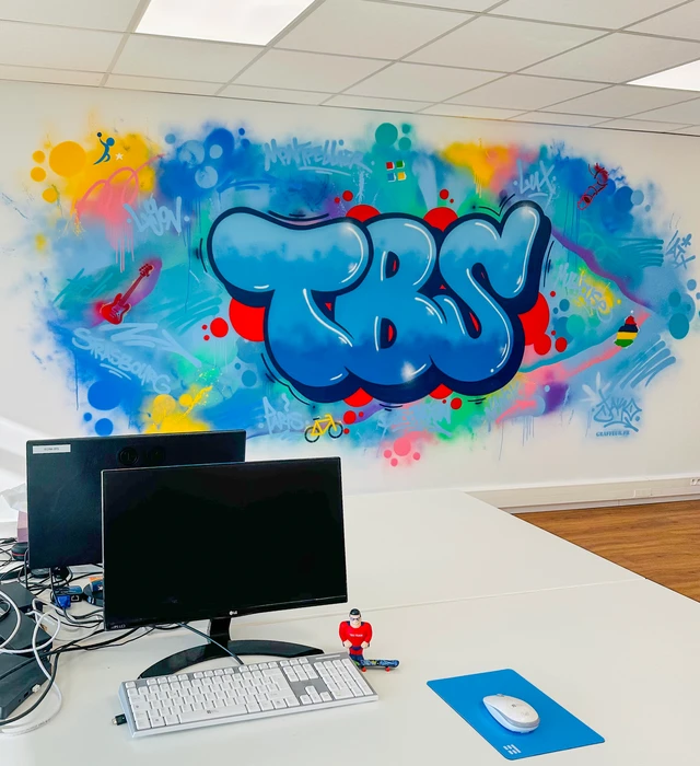Photographie d'une fresque murale de grande dimension réalisée en environnement professionnel (hall d'accueil d'entreprise, façade de bâtiment commercial ou couloir de local professionnel), montrant une composition artistique moderne et colorée avec des motifs géométriques ou des lettres stylisées peintes à la main, démontrant la maîtrise technique et la créativité du street art, avec un rendu de qualité photographique professionnelle montrant clairement le détail et la finition du travail.